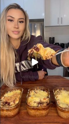 a woman is holding up some food in front of three dishes on a table with one hand