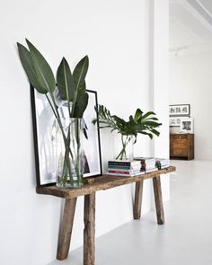 a wooden table topped with plants next to a white wall