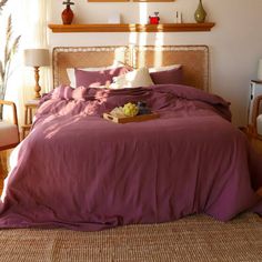 a bed with purple sheets and pillows in a bedroom next to two lamps on either side of the bed