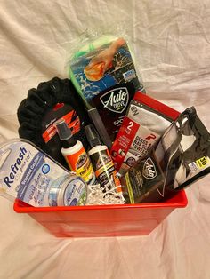 a red basket filled with lots of items on top of a white sheet covered bed