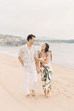 a man and woman are walking on the beach holding each other's hands as they smile