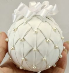 a hand holding a white ornament with pearls and bows on it's side