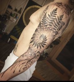 a man's arm covered in black and white tattoos with fern leaves on it