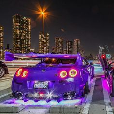 two purple sports cars parked next to each other in front of a cityscape