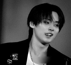 black and white photo of a young man with short hair, wearing a necklace that has a camera on it