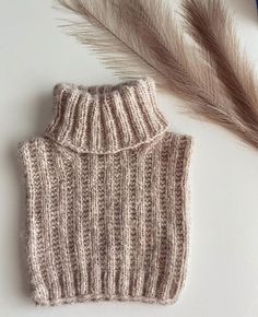 a knitted sweater sits next to some feathers