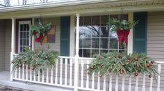 two christmas wreaths hanging from the front porch of a house with evergreen and red berries