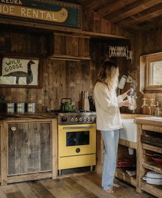 a woman standing in a kitchen next to a yellow stove top oven and wooden cabinets