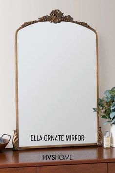 a mirror sitting on top of a wooden dresser next to a vase and potted plant