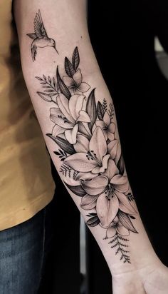 a woman's arm with flowers on it and a bird flying over the top