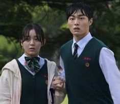 two young men standing next to each other wearing green vests and bow ties with trees in the background