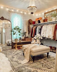 a bedroom with a bed, ottoman and closet full of clothes on hangers next to a chandelier