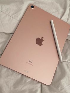 an apple ipad with a pen on top of it sitting on a bed next to some sheets