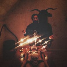 a man and woman in the middle of a table with candles on it, surrounded by devil horns