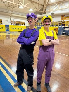 two men in costumes standing on a basketball court with their arms crossed and one wearing a purple shirt