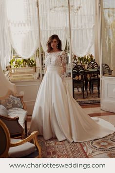 a woman standing in front of a window wearing a wedding dress with long sleeves and an open back