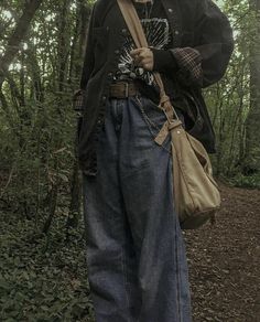 a man standing in the woods with a bag on his shoulder and an umbrella over his head