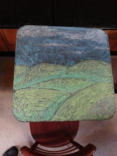 a wooden chair with a painting on the back of it's seat next to a pair of black shoes