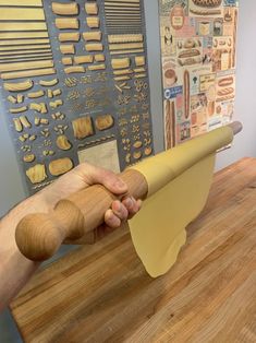 a person holding a piece of yellow paper on top of a wooden table next to a poster