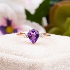 an amethorate and diamond ring sitting on top of a white cloth with flowers in the background