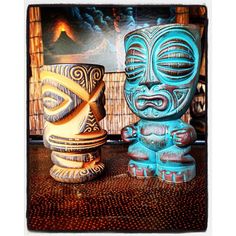 two wooden tiki statues sitting on top of a table next to each other in front of a painting