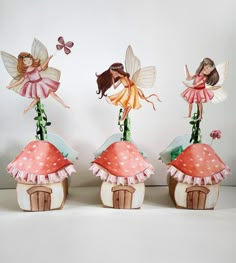 three little fairy figurines sitting on top of mushroom houses with flowers and butterflies