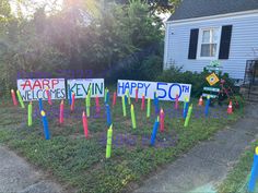 several yard signs in front of a house with trees and bushes behind them that say happy 50th