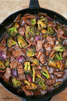 beef and broccoli stir fry in a skillet on a wooden counter top