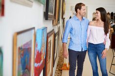 a man and woman standing next to each other in front of paintings on the wall