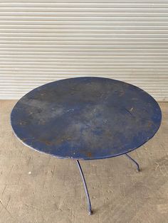 a round metal table sitting on top of a cement floor next to a garage door