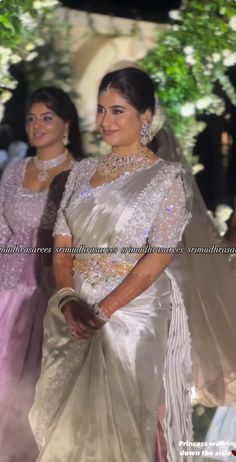 two women in dresses standing next to each other at a wedding ceremony with flowers and greenery behind them