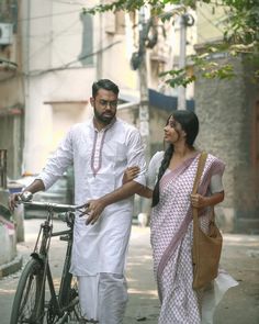 a man and woman walking down the street next to a bike