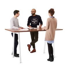 three people are sitting at a table and one person is standing up with his feet on the desk