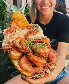 a woman is holding up a plate of food with shrimp, rice and pineapple