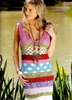 a woman wearing a colorful crochet dress standing in front of water