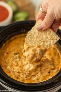 a hand dipping a tortilla chip into a slow cooker filled with salsa