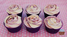 six cupcakes with white frosting on a pink table