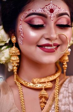 a woman wearing gold jewelry and makeup with flowers in the background