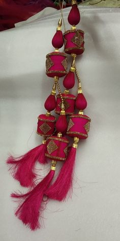 a pink and gold necklace with tassels hanging from it's side on a white surface