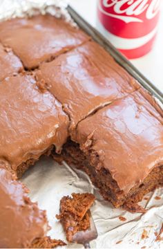 a piece of chocolate cake on top of aluminum foil with coca - cola can in the background