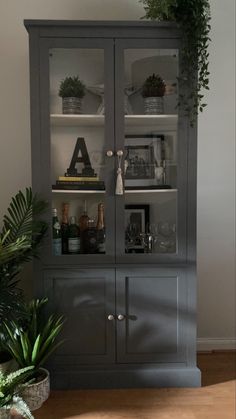 a gray china cabinet with glass doors and plants