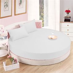 a round bed with orange sheets and pillows on top of it in a pink room