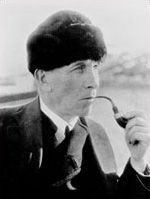 black and white photograph of a man in suit holding a pipe to his mouth while looking at the camera