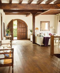 a living room filled with furniture and wooden beams on the ceiling, next to a doorway