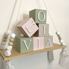 a wooden shelf with letters and tassels hanging from it's sides in front of a white wall