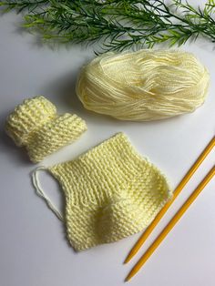 two knitted mittens, one yellow and the other white next to a pair of knitting needles