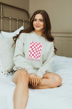 a woman sitting on top of a bed wearing a sweatshirt