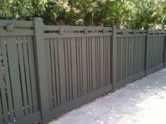 a fence that is next to a sidewalk with trees and bushes in the back ground