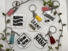 six glass key chains with words and tassels hanging from them on a white surface