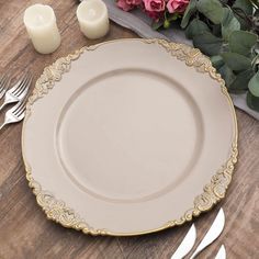 a white and gold dinner plate with silverware next to it on a wooden table